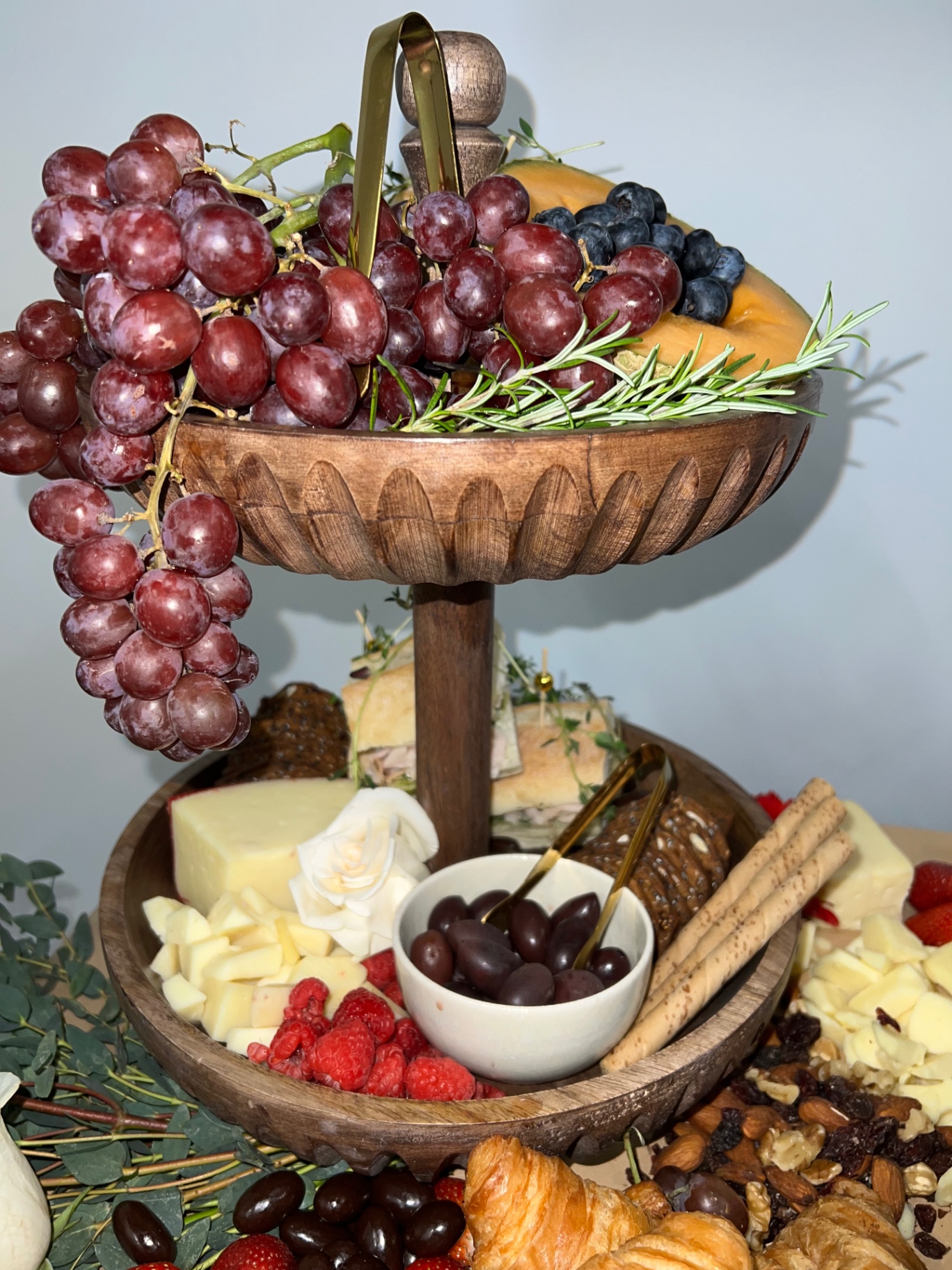 Two-tier wooden stand with grapes, cheeses and tea sandwiches